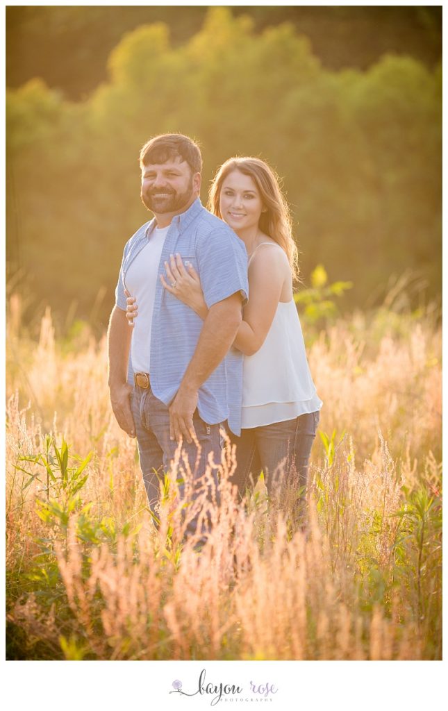 Couple posing in field for engagement photos at sunset