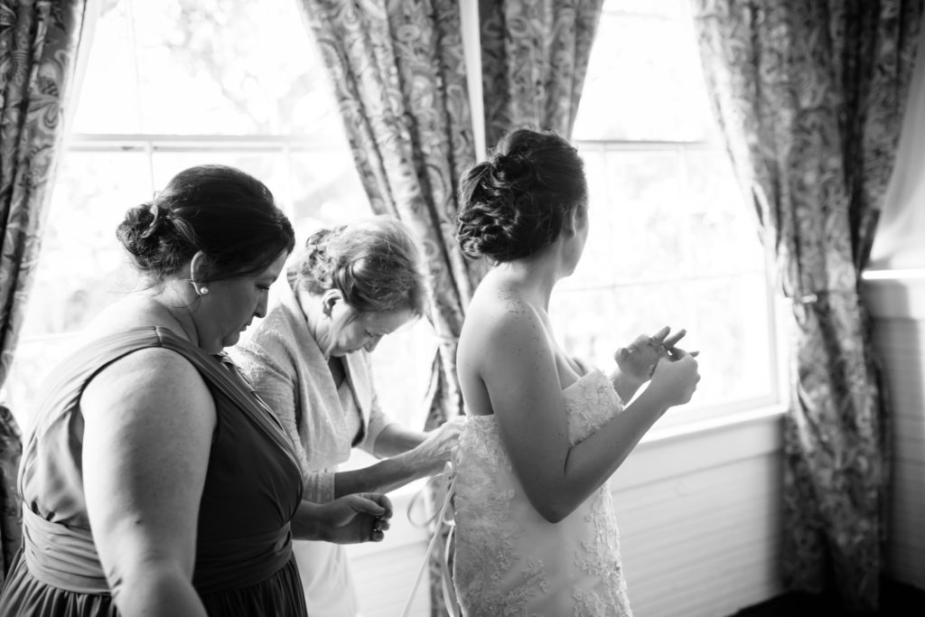 Bride being dressed by mother taken by second photographer