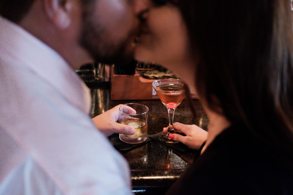 Couple kissing in bar holding cocktails