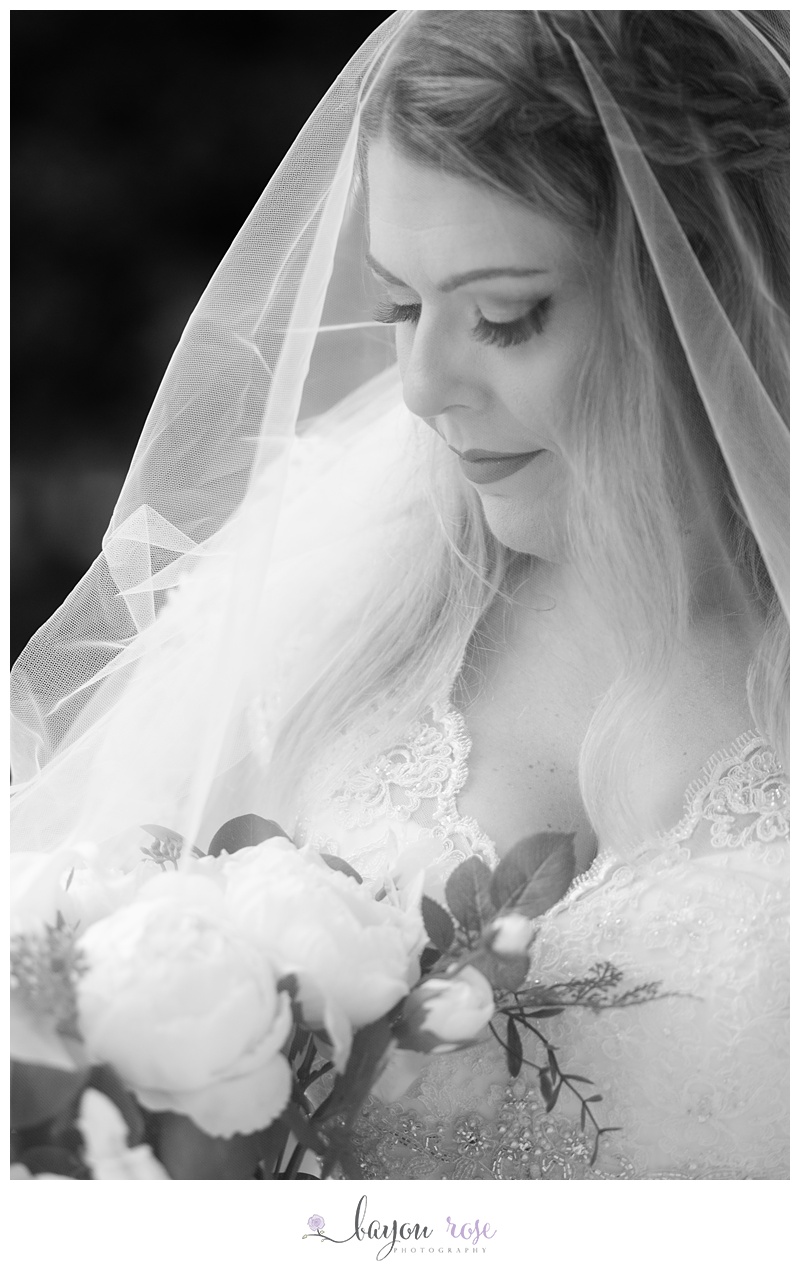 Black and white image of bride with veil over face, holding flowers