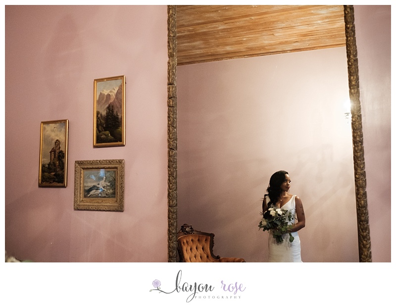 Bride poses in wedding dress against pink wall, holding bouquet with antique paintings on the wall of Blythewood Plantation