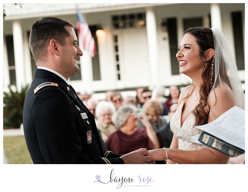Couple smiles at each other happily while exchanging rings during Baton Rouge backyard wedding
