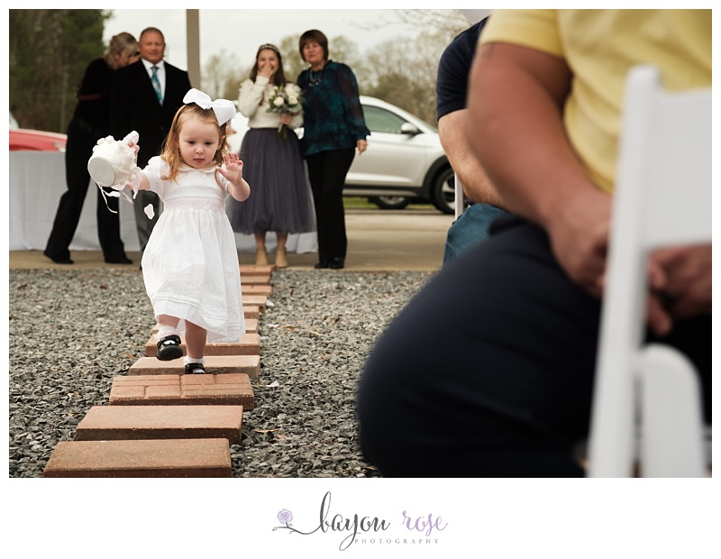 flower girl concentrates while walking down aisle as bride watches and laughs