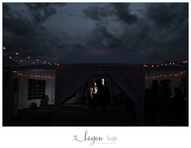 bride and groom under tent laughing, while storm clouds are overhead