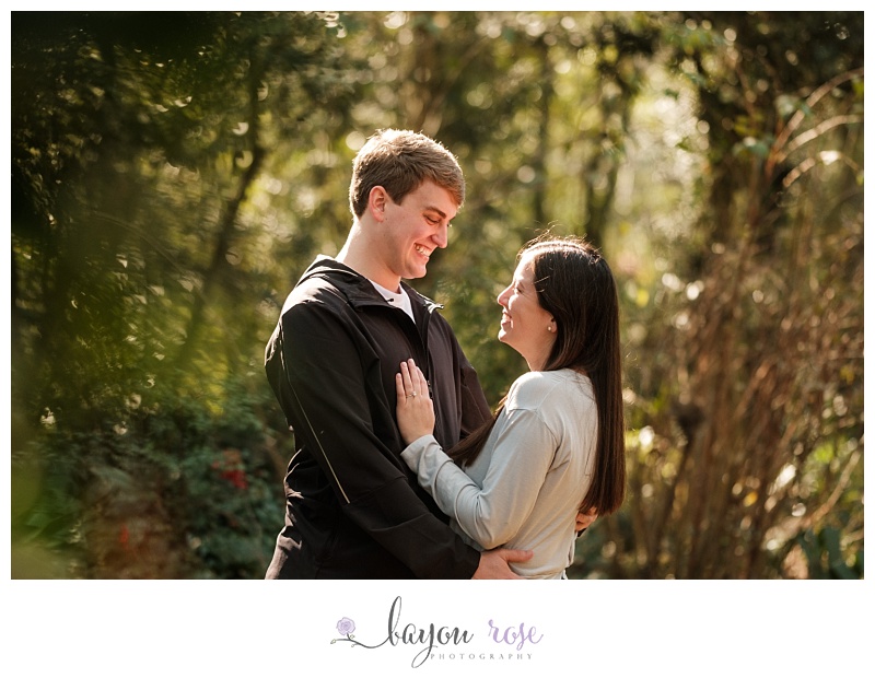 image of engaged couple against trees laughing in sunlight after proposal photography session