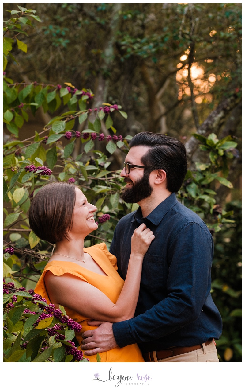 Couple posing for engagement photo in bushes at sunset on LSU campus