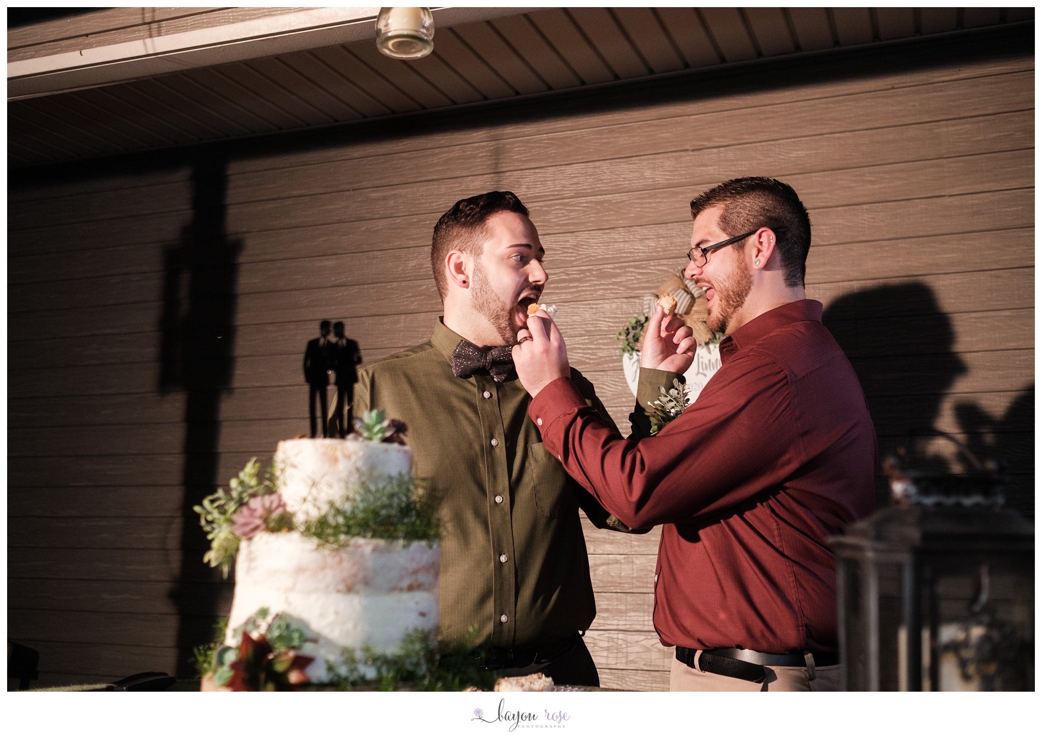two grooms feeding each other cake at wedding reception