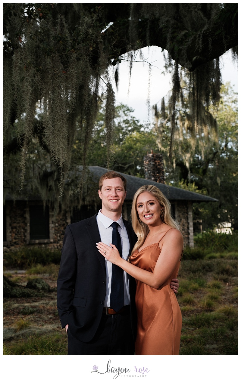 Engaged couple smiling in front of cottage with spanish moss