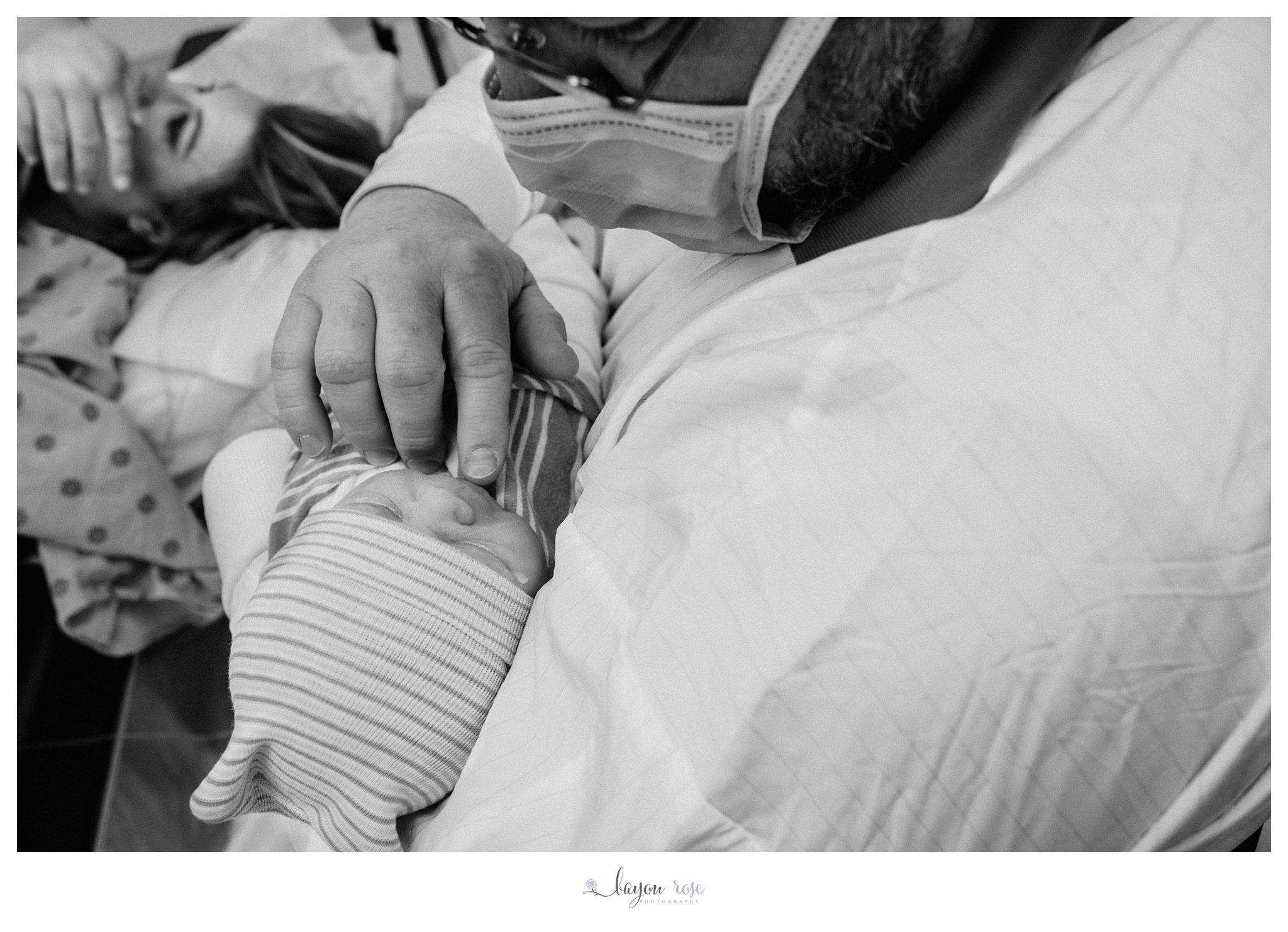 dad touches baby girl's chin as mom wipes tears from her eyes after giving birth